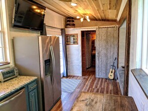 A kitchen with a refrigerator, microwave, and toaster, leading to a wooden interior and a guitar. - Tiny House with Amazing Views and Private Hiking Trails in Hill Country, Texas (Pipe Creek)
