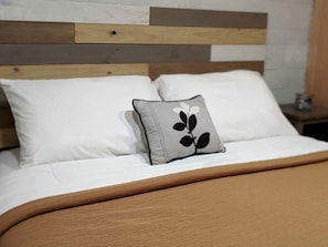 A bed with a wooden headboard, white bedding, and a single decorative pillow. - Tiny House with Amazing Views and Private Hiking Trails in Hill Country, Texas (Pipe Creek)