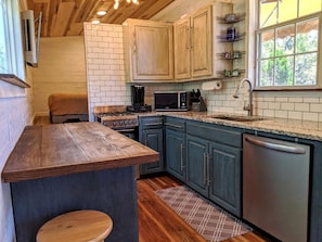 A kitchen with wooden cabinets, a countertop, a stove, a microwave, and a dishwasher. - Tiny House with Amazing Views and Private Hiking Trails in Hill Country, Texas (Pipe Creek)