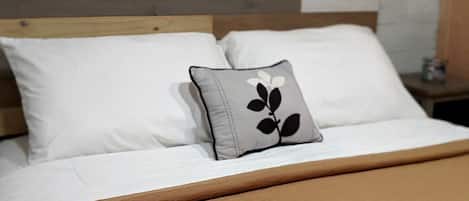 A bed with a wooden headboard, white bedding, and a single decorative pillow.