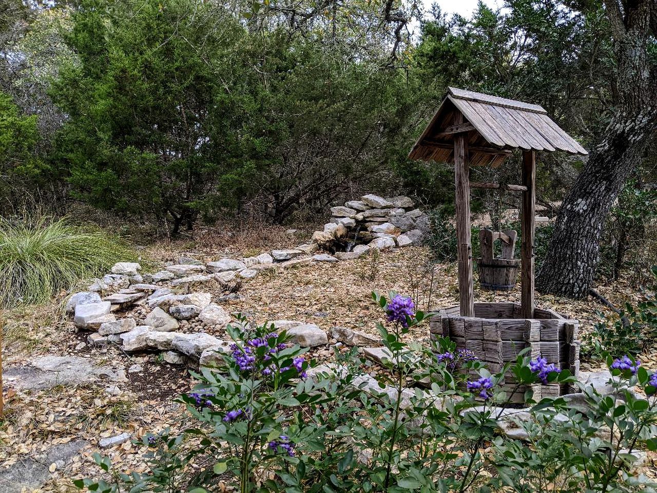 Une construction rustique en bois, dotée d’un toit incliné et entourée de rochers et de feuillage.