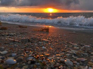 Ein Strand mit Kieselsteinen und Wellen bei Sonnenuntergang.