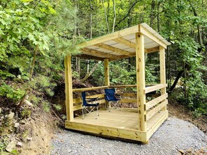 A wooden gazebo with a roof, two blue folding chairs, and a gravel ground. - Cozy and Rustic Cabin Rental in the Smokies for Romantic Getaways in Tennessee (Newport)