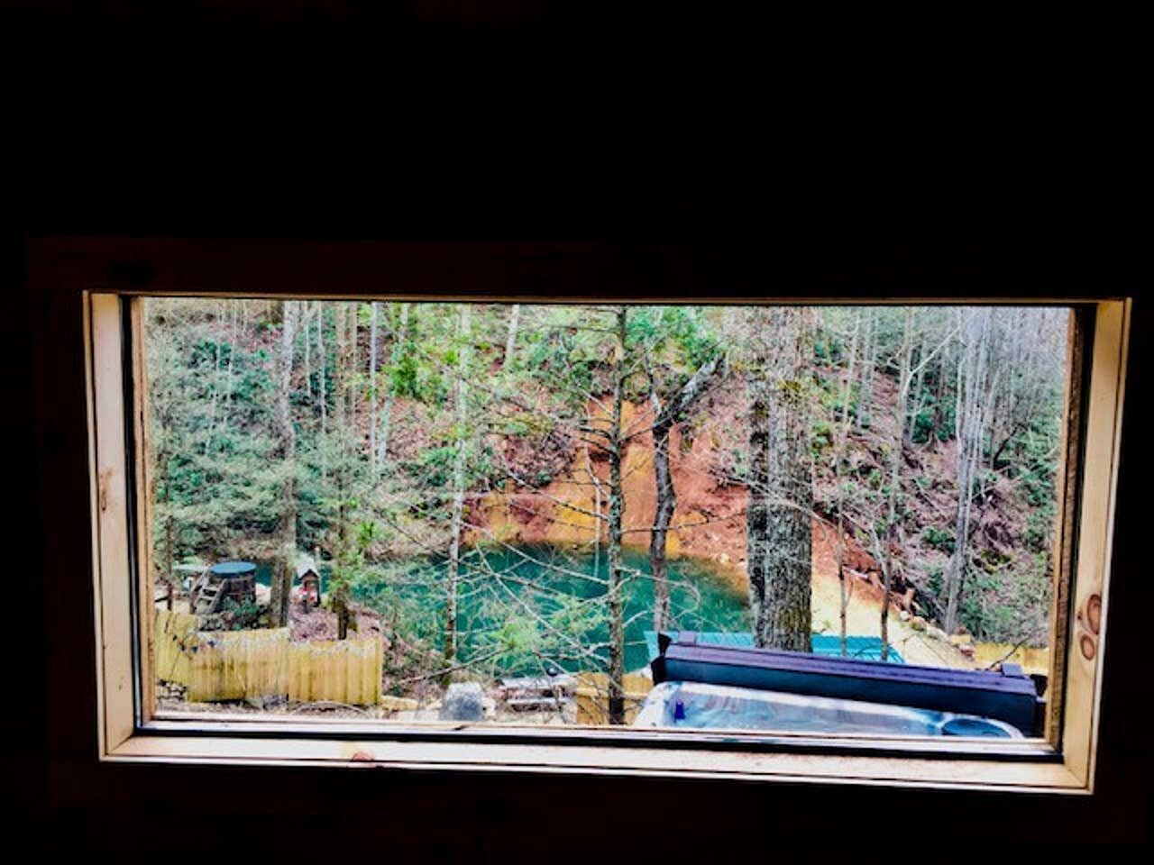 A window view of a forested area with a wooden fence and a small structure.