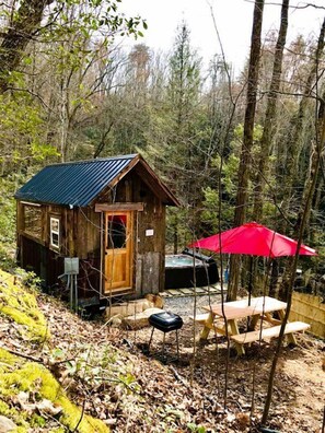 A rustic cabin with a wooden door, a small porch, and a red umbrella. - Cozy and Rustic Cabin Rental in the Smokies for Romantic Getaways in Tennessee (Newport)