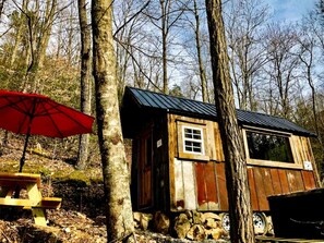 A rustic cabin with a small window, a red umbrella, and a wooden bench. - Cozy and Rustic Cabin Rental in the Smokies for Romantic Getaways in Tennessee (Newport)