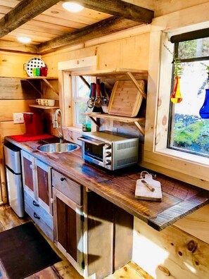 A compact kitchen with a sink, microwave, and wooden cabinets. - Cozy and Rustic Cabin Rental in the Smokies for Romantic Getaways in Tennessee (Newport)