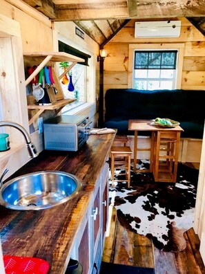 A compact kitchen with a sink, wooden cabinets, a window, and a cowhide rug. - Cozy and Rustic Cabin Rental in the Smokies for Romantic Getaways in Tennessee (Newport)