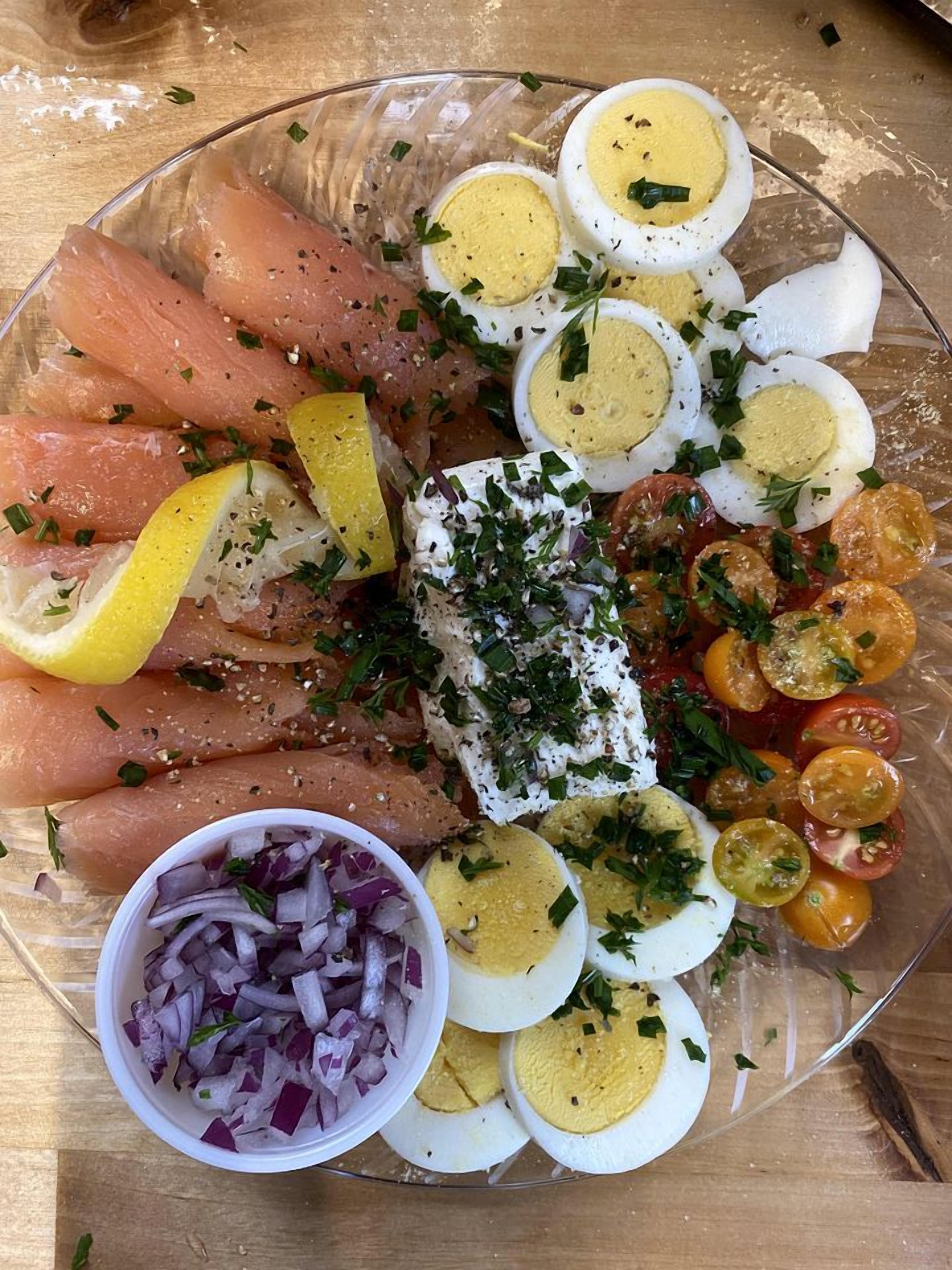 A glass plate with sliced salmon, hard-boiled eggs, cherry tomatoes, and a small bowl of red onion.