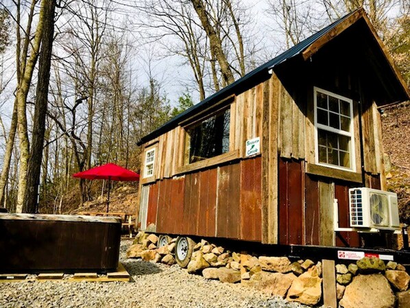 A rustic cabin with a stone foundation, a red umbrella, and an air conditioning unit. - Cozy and Rustic Cabin Rental in the Smokies for Romantic Getaways in Tennessee (Newport)