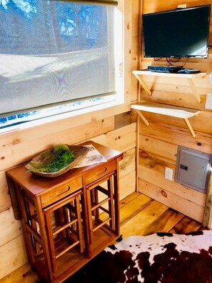A wooden cabin interior with a window, a television, a small table with a bowl, and a cowhide rug. - Cozy and Rustic Cabin Rental in the Smokies for Romantic Getaways in Tennessee (Newport)