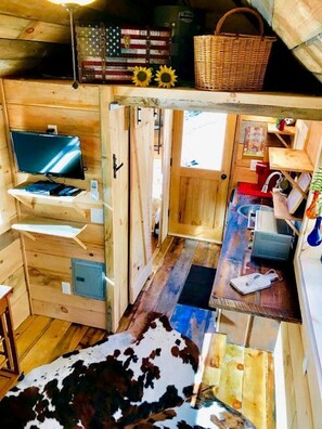 A compact wooden cabin with a television, a small kitchen area, and a cowhide rug. - Cozy and Rustic Cabin Rental in the Smokies for Romantic Getaways in Tennessee (Newport)