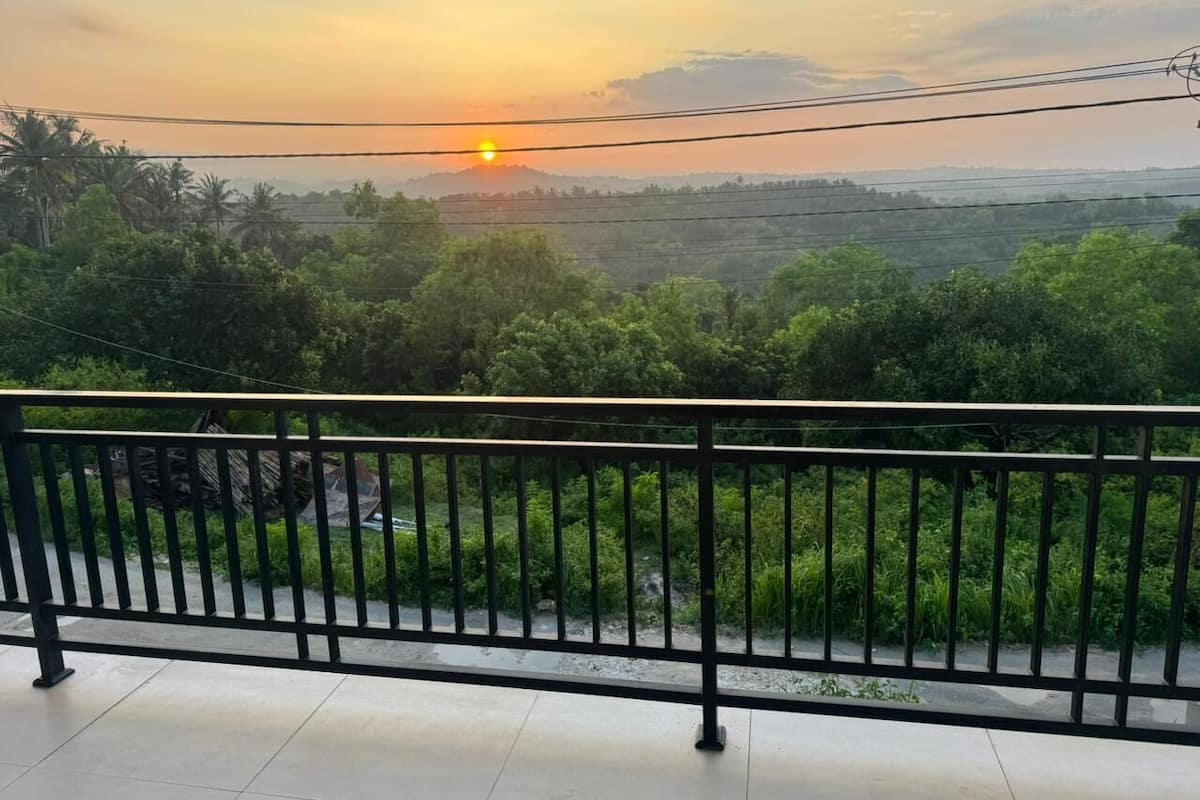 A balcony with a metal railing overlooking a lush green landscape during sunset.