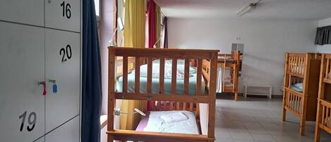 A dormitory room with bunk beds, a desk, a chair, a small stool, and a wardrobe with numbered compartments.