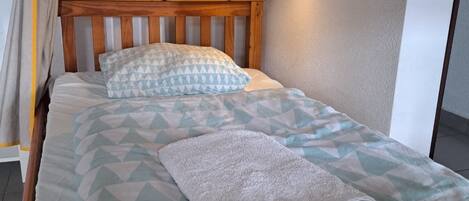 A single bed with a geometric patterned bedspread, a wooden headboard, and a white towel folded on the bed.