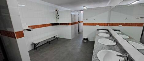 Eine öffentliche Toilette mit weißen Fliesen, einer Sitzbank und einer langen Ablage mit mehreren Waschbecken.