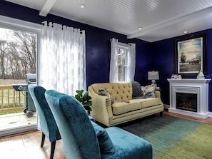 A living room with a sofa, two armchairs, a fireplace, and a large window with curtains. - Elegant Farm Cottage Rental for a Countryside Getaway near Lancaster, Pennsylvania (Columbia)