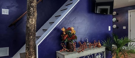 Un escalier avec une rampe métallique, un mur bleu foncé, un plancher en bois, une console ornée d’objets décoratifs et une plante en pot.
