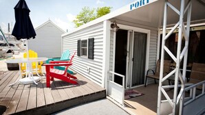 Un espace extérieur abrité, équipé d’une table et de chaises, une porte donnant sur une pièce, et une pancarte indiquant « PORT ».
