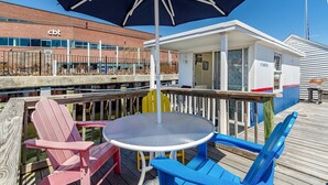 Une terrasse en bois avec une table ronde et des chaises, un grand parasol, et un bâtiment avec une enseigne indiquant « cbt » en arrière-plan.