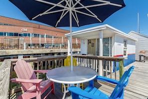 A wooden deck with a round table and chairs, a large umbrella, and a building with 'cbt' signage in the background.