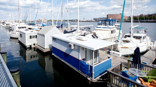 Un port de plaisance où sont amarrés de nombreux bateaux, un bâtiment à la façade bleue et blanche, et un ciel dégagé.