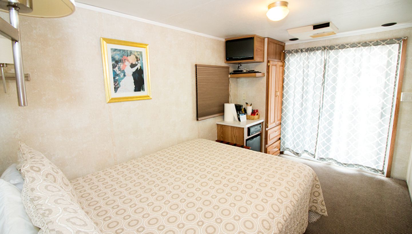 Un dormitorio con cama, mesita de noche, televisor, armario y ventana con cortinas.