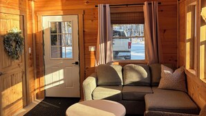 A log cabin interior with a sofa, a small table, and a door leading outside.