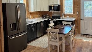 A compact kitchen with a refrigerator, stove, microwave, and white cabinets.
