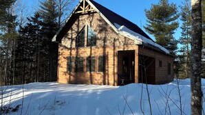 A wooden cabin with a gabled roof, large windows, and a snow-covered ground.
