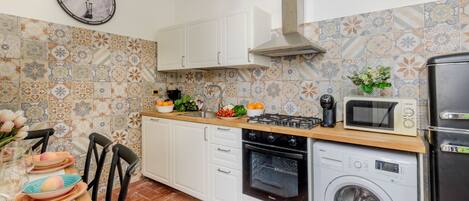 A compact kitchen with white cabinets, a microwave, a washing machine, and a clock on the wall.