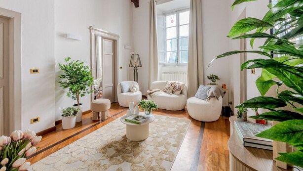 A cozy living room with a wooden ceiling, a large window with shutters, a white sofa, a coffee table, and several potted plants. - The Gallo Promenade in Lucca (Lucca)