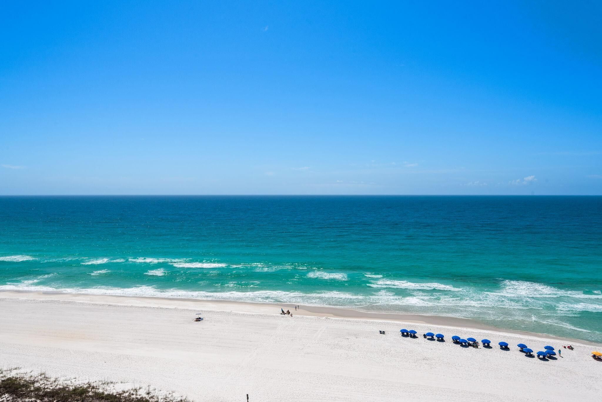 A beach with a row of blue umbrellas and a sandy shore.