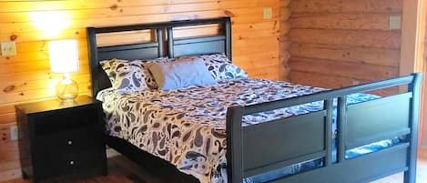 Quarto de cabana de madeira com cama, mesa de cabeceira e luminária na parede.