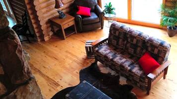 L'intérieur d'une cabane en rondins, avec un fauteuil en cuir, un canapé à motifs, une petite table et un tapis en peau de vache.