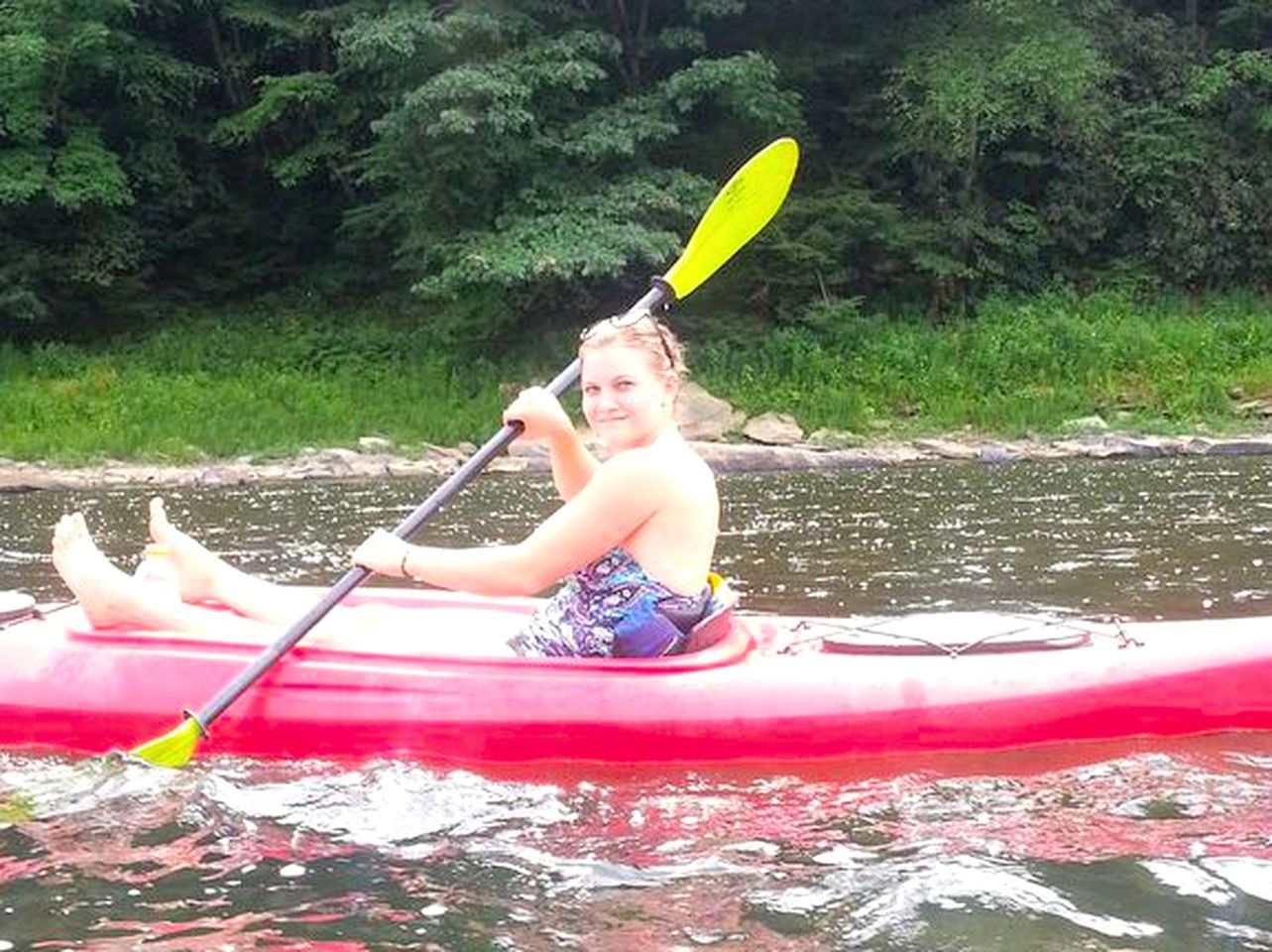 A person in a red kayak on a body of water with greenery in the background.
