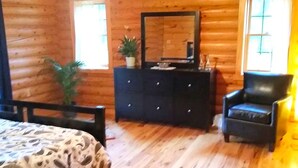 L’intérieur d’un chalet en bois, avec un lit, une commode, une chaise et un grand miroir.
