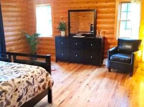 A wooden cabin interior with a bed, dresser, chair, and a large mirror.