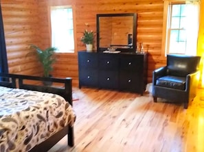 A wooden cabin interior with a bed, dresser, chair, and a large mirror.