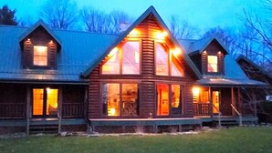 Une cabane en rondins dotée d’une grande fenêtre centrale, de plusieurs petites fenêtres et d’un porche.