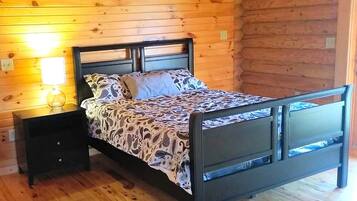 A wooden cabin bedroom with a bed, nightstand, and wall-mounted lamp.