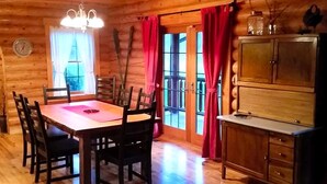 L’intérieur d’un chalet en bois comprend une table à manger, des chaises, un lustre, un buffet et une fenêtre avec des rideaux.