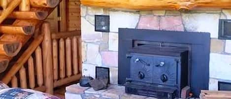 Ein Kamin aus Stein mit einem schwarzen Holzofen, einem Holzscheitenlager und einem Sofa mit Karomuster.