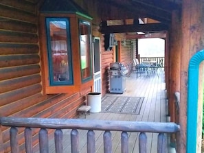 A wooden cabin with a porch, a grill, and a trash can.