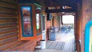 Une cabane en bois avec une véranda, un barbecue et une poubelle.