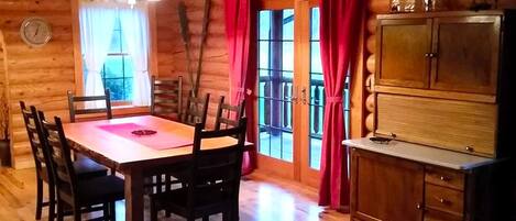 L’intérieur d’un chalet en bois comprend une table à manger, des chaises, un lustre, un buffet et une fenêtre avec des rideaux.