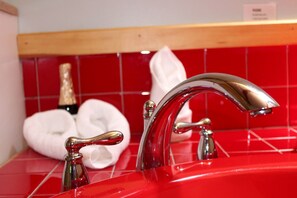 A red bathroom sink with chrome fixtures and a red tiled backsplash.