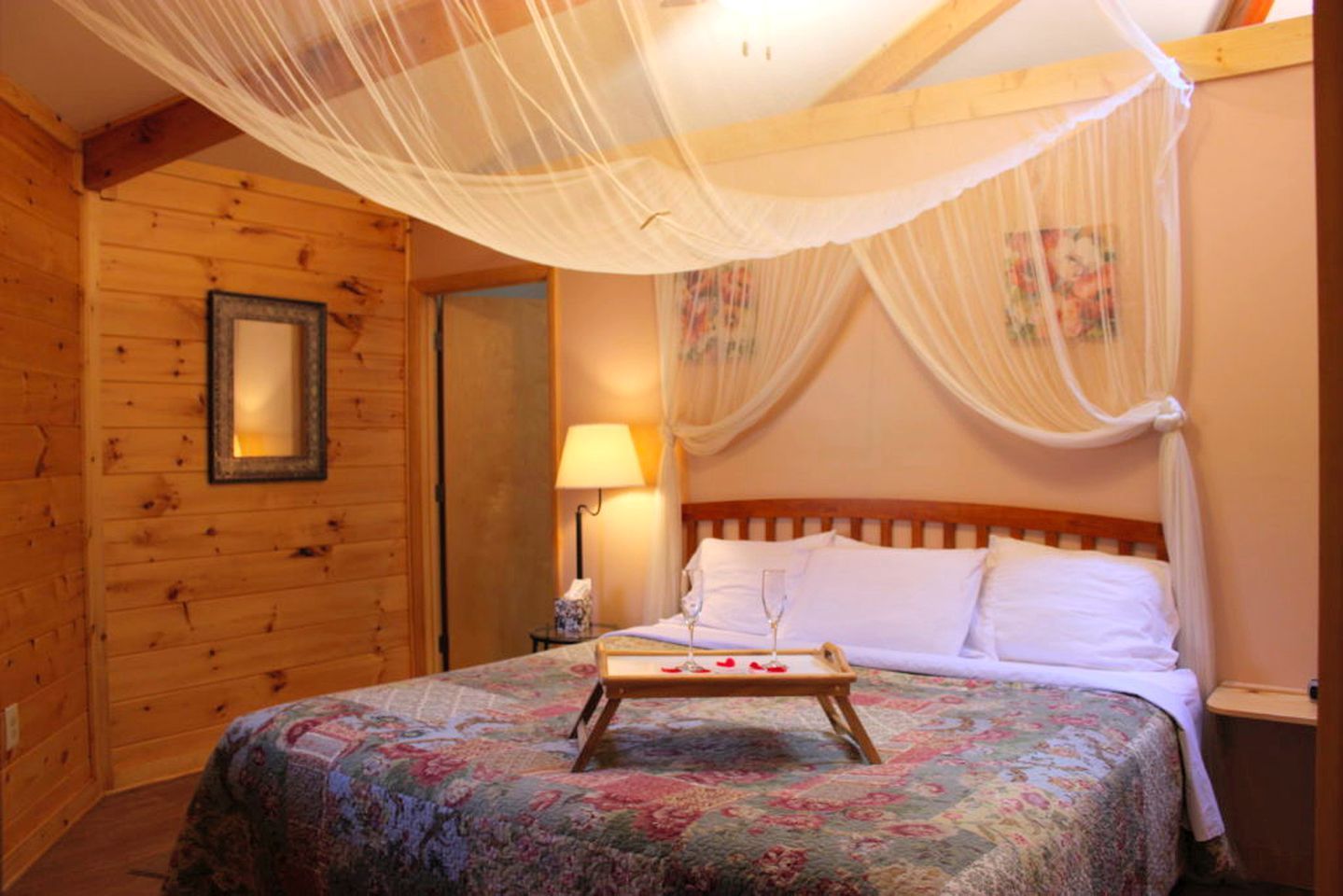 Ein Zimmer aus Holz mit einem Bett, einem Nachttisch, einer Lampe und einem Baldachin.