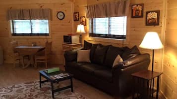 A cozy log cabin interior with a leather sofa, a small table, a lamp, and a dining area.