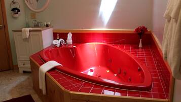 Eine rote Badewanne in einem Badezimmer mit einer Holzbank, einem weißen Handtuch und einer kleinen Vase mit Blumen.